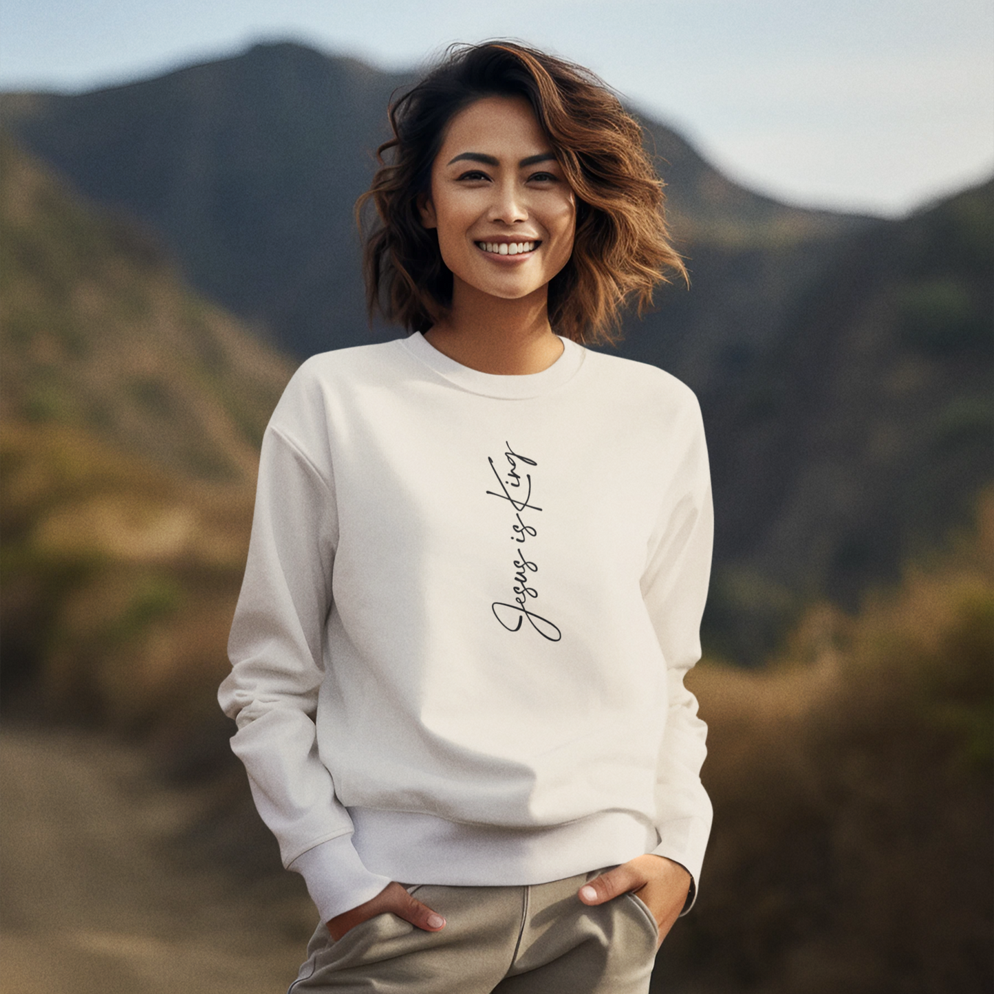Woman wearing a ivory sweatshirt with text standing in front of mountains