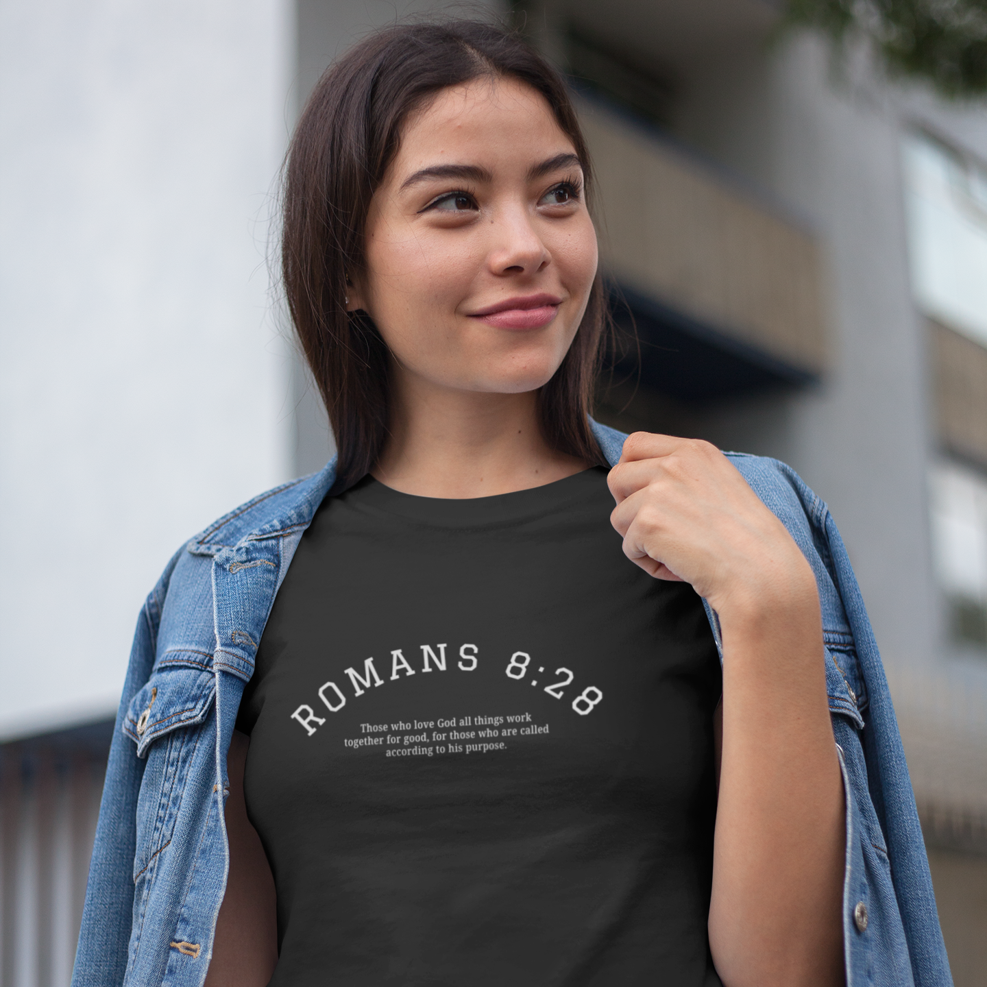 Woman wearing a black t-shirt with 'ROMANS 8:28' text, standing outdoors.