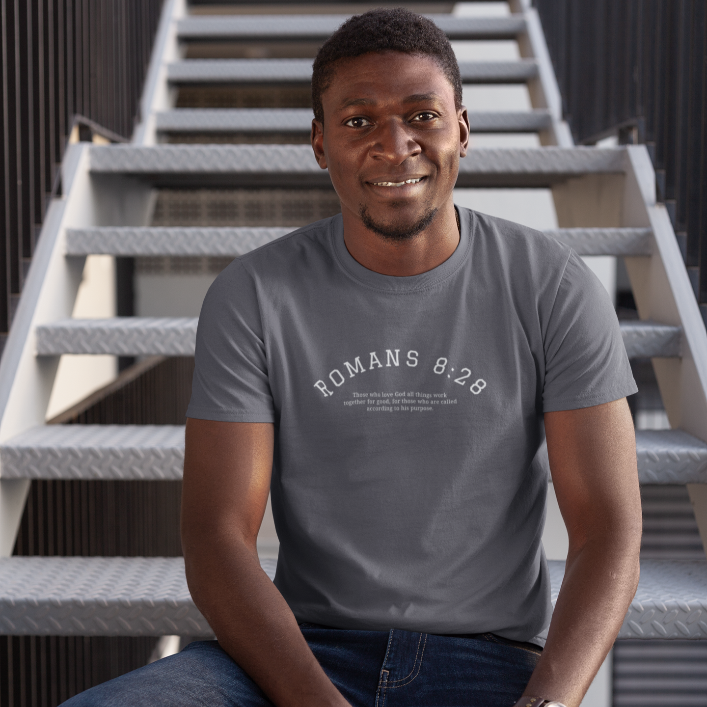 Man wearing a gray t-shirt with text sitting on metal stairs.