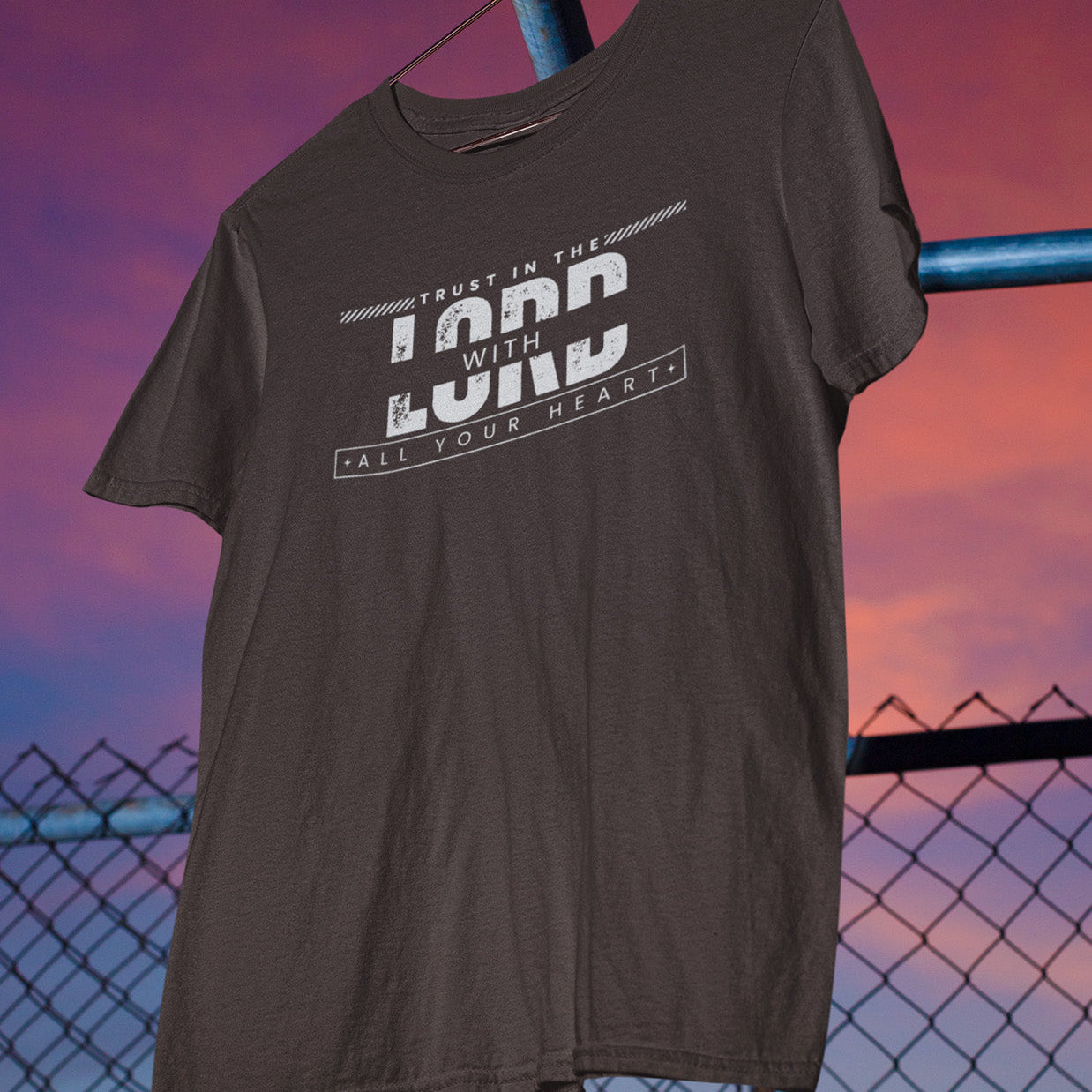 Brown t-shirt with text design hanging against a sunset sky.