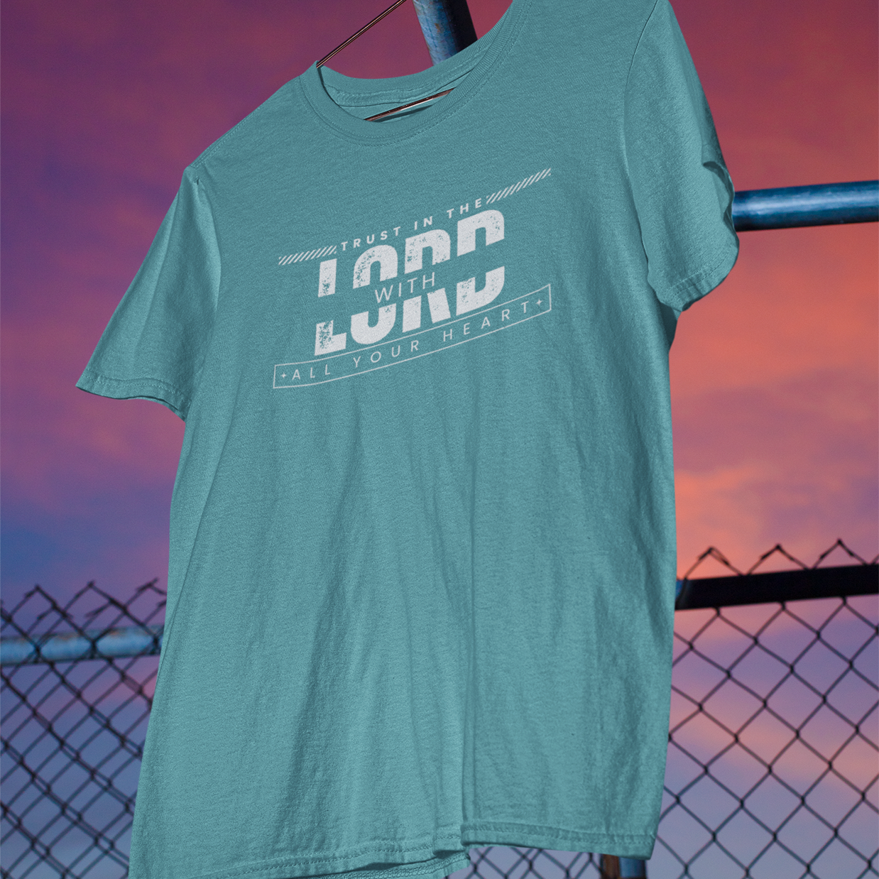 Teal t-shirt with text design hanging against a sunset sky.