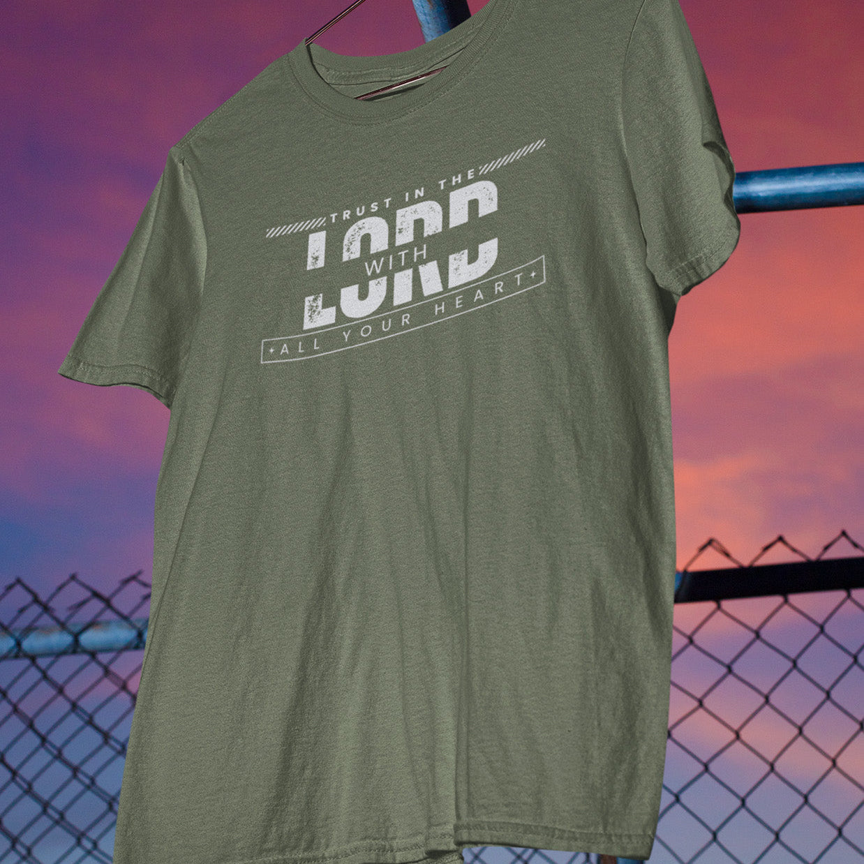 Green t-shirt with text design hanging against a sunset sky.