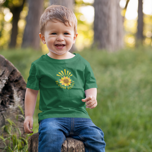 Child wearing a green t-shirt with a sunflower design, sitting on a log in a forest.