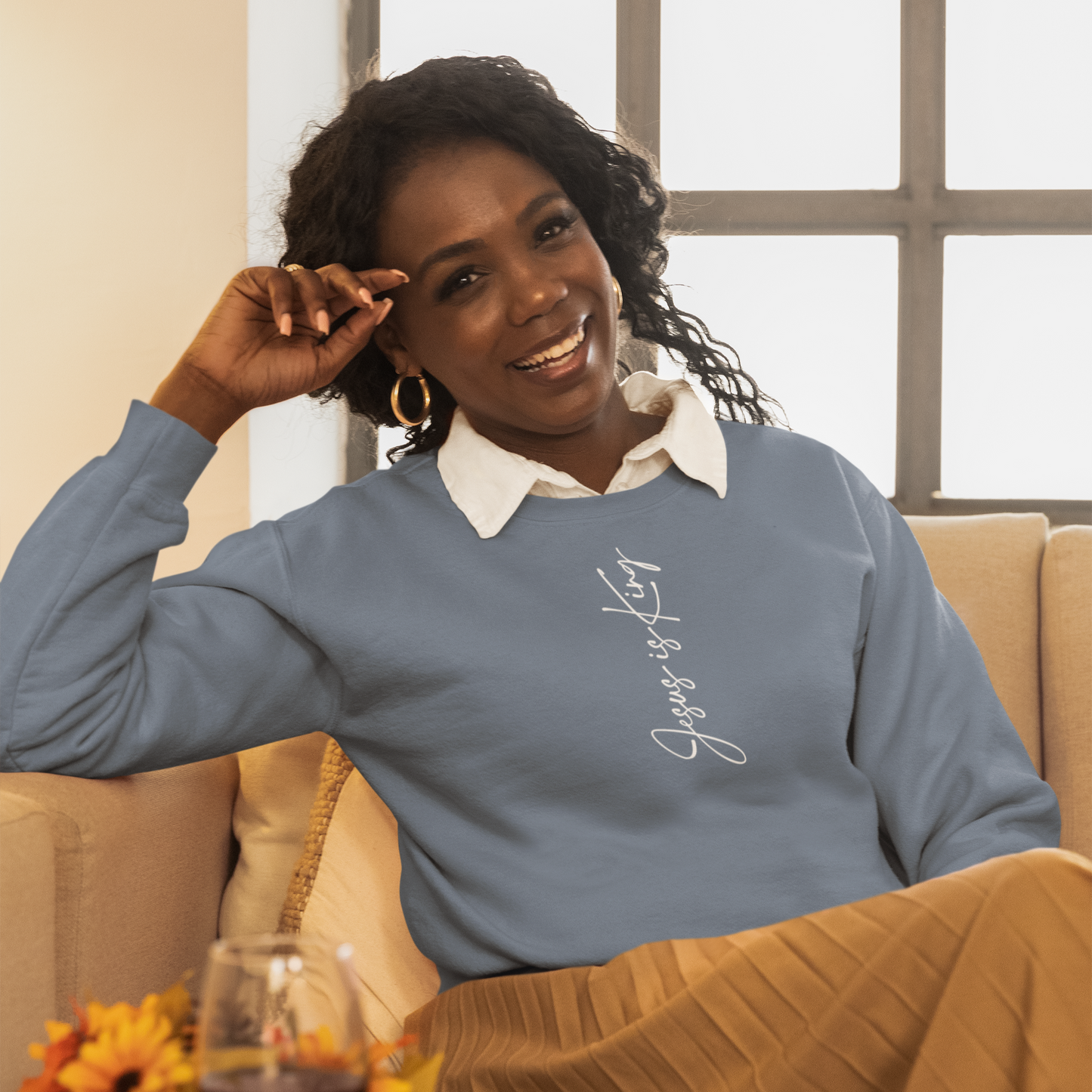 Woman sitting on a couch wearing a blue sweater with text, smiling.