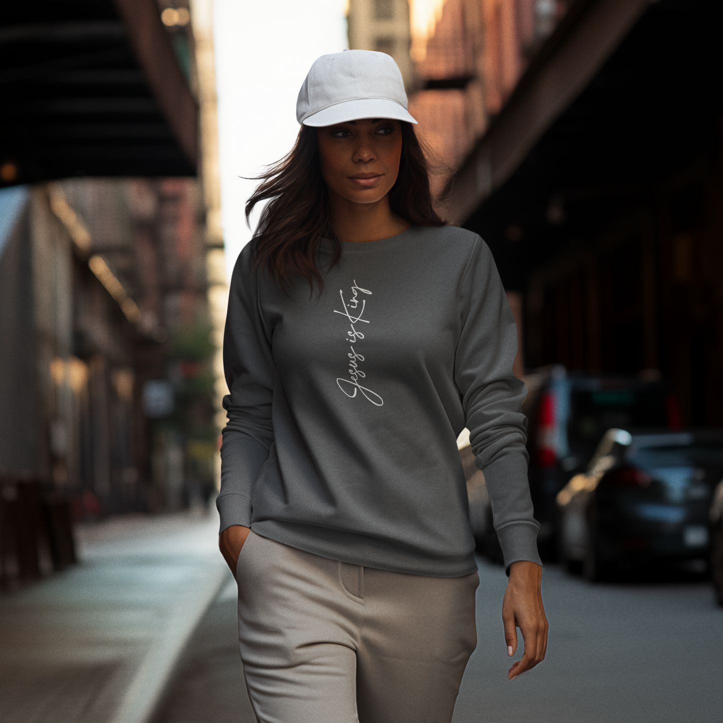 Woman walking on a street wearing a pepper sweatshirt and white cap.