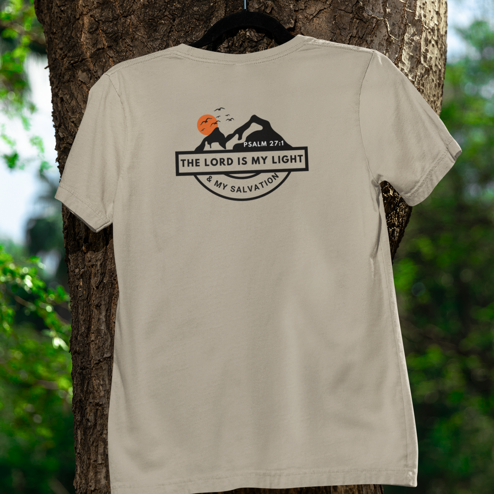 Beige t-shirt with a graphic design and text on the back, hanging on a tree