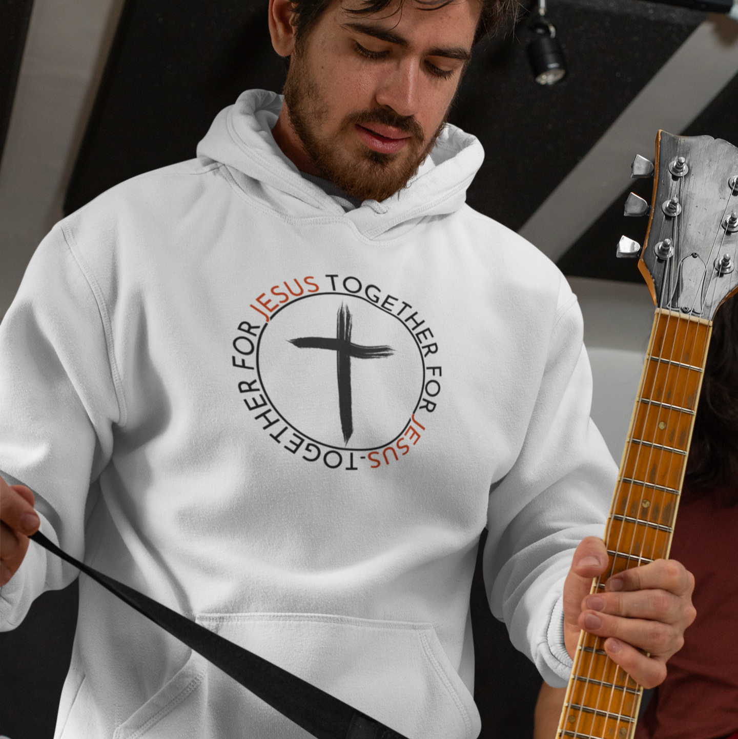 Man wearing a white hoodie with a cross design holding a guitar