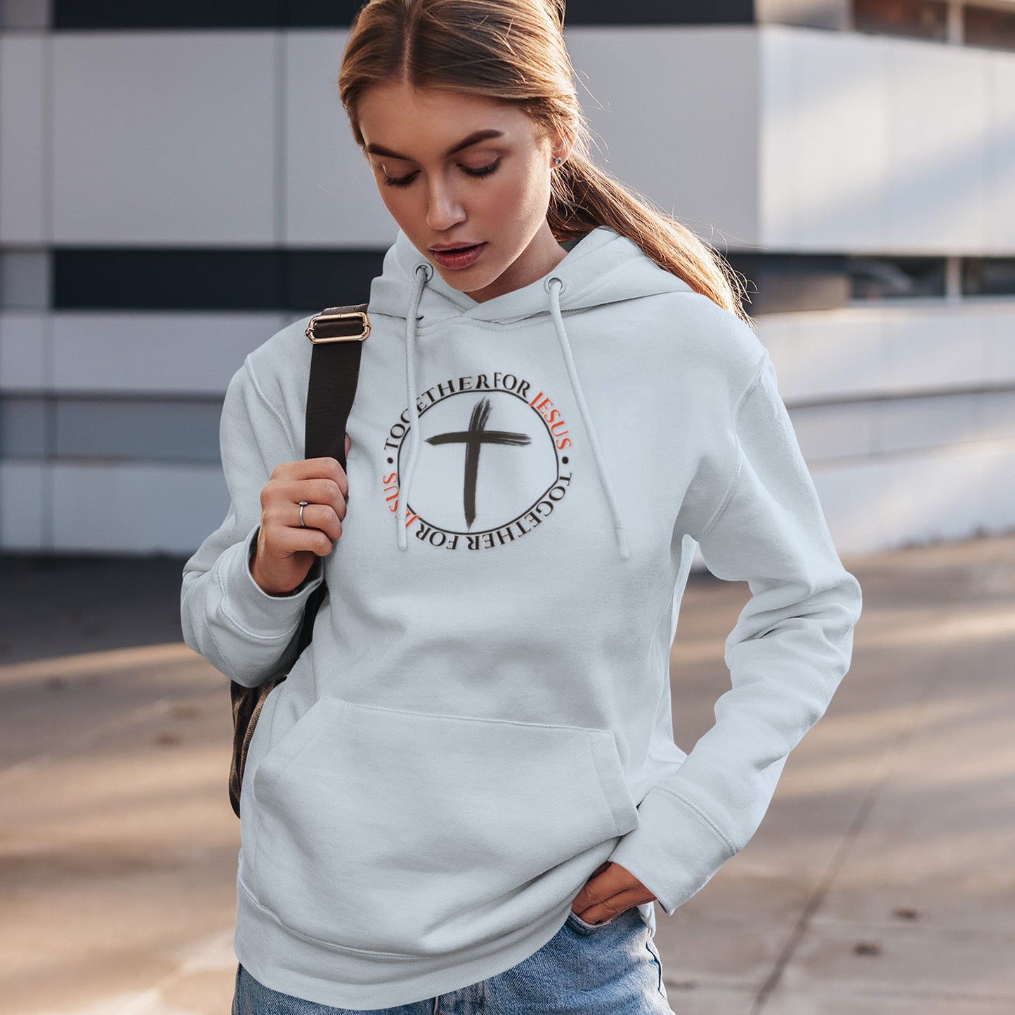 Woman wearing a white hoodie with a cross design and text, standing outdoors.