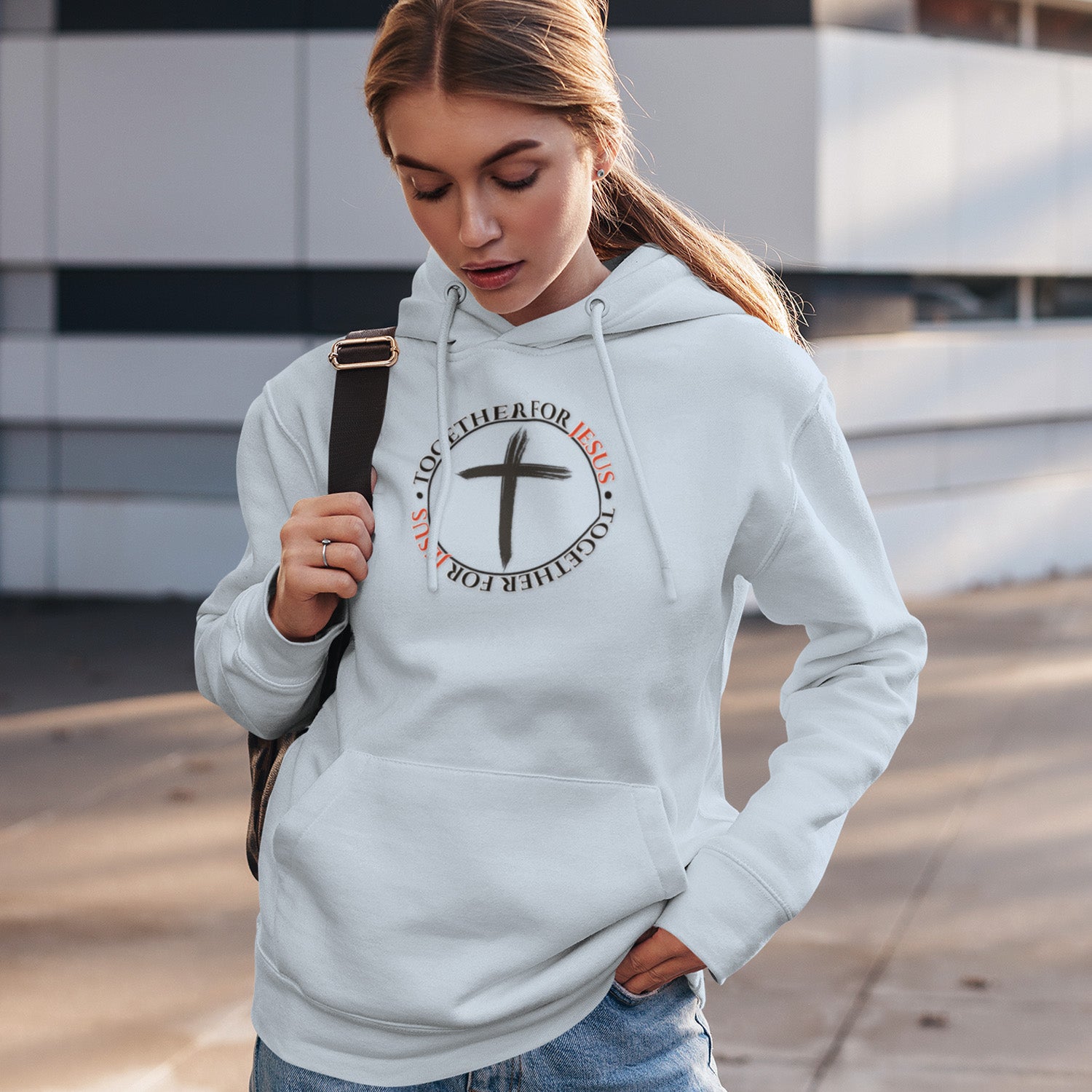 Woman wearing a white hoodie with a cross design and text, standing outdoors.