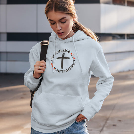 Woman wearing a white hoodie with a cross design and text, standing outdoors.